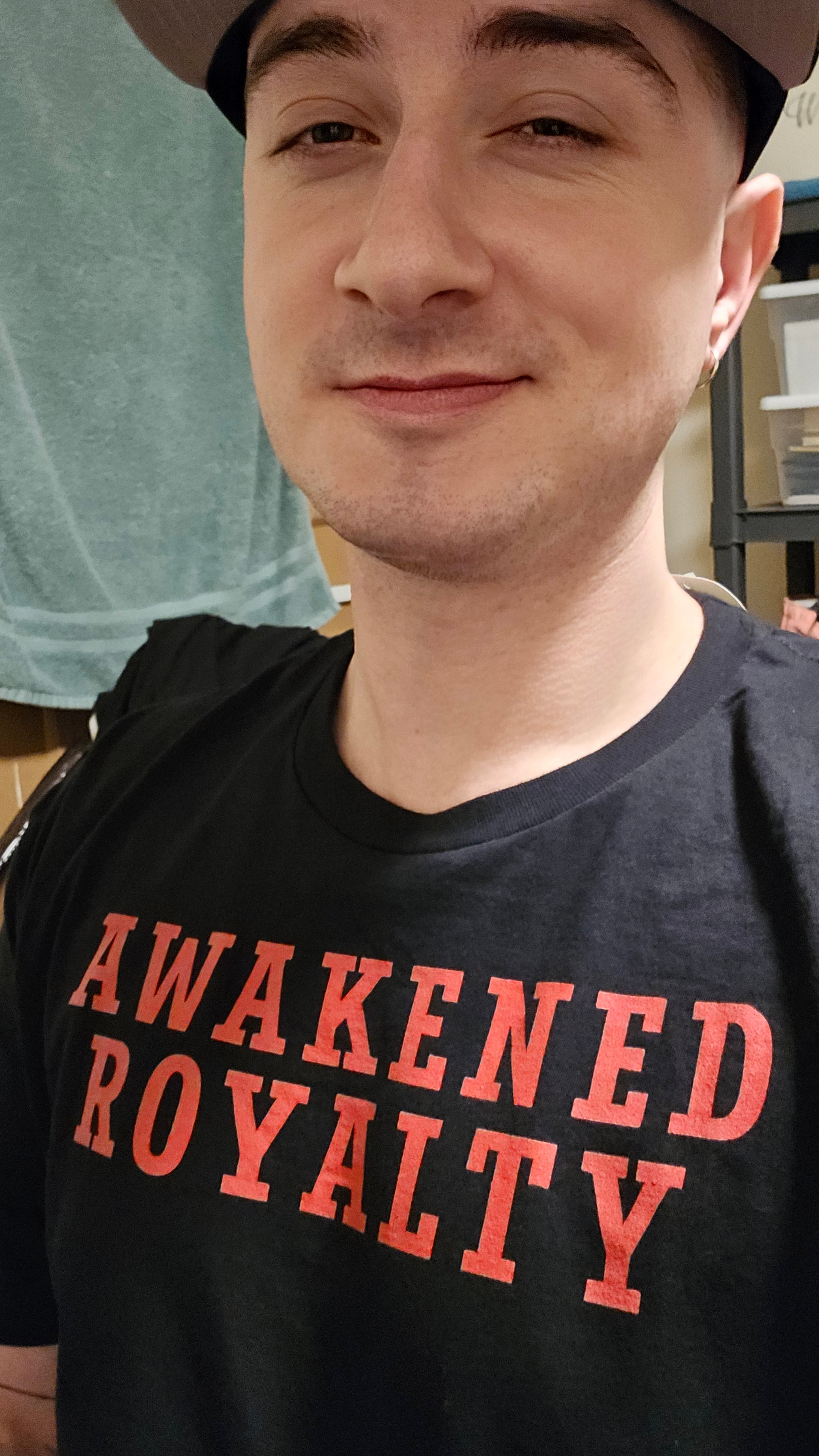 Person wearing a black t-shirt with red text 'Awakened Royalty' in an indoor setting.